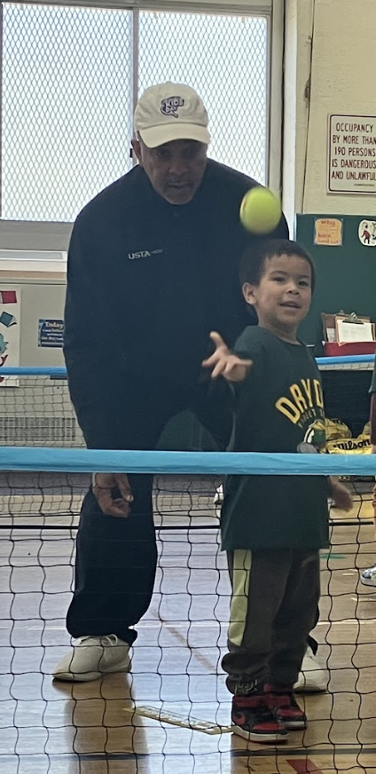 young boy throws a tennis ball with a coach